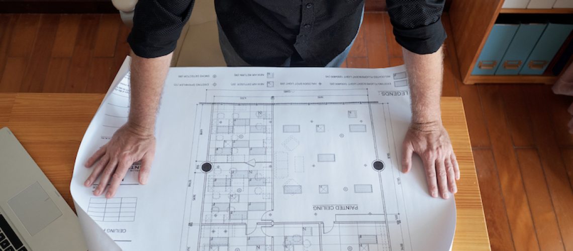 High angle view of unrecognizable mature man looking at large blueprint of ceiling while standing near office desk